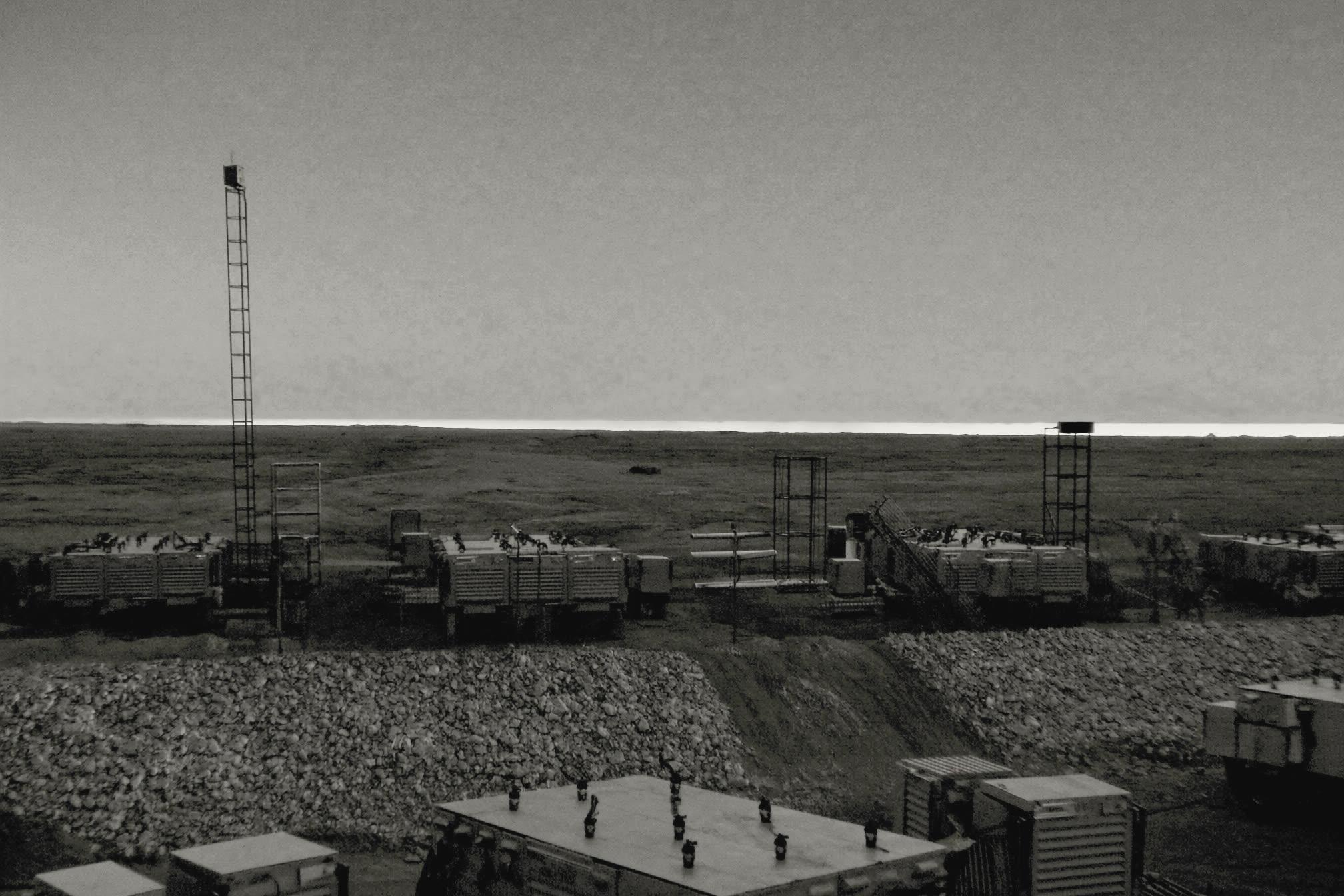 Rows of unbranded modular generator enclosures and exhaust stacks on a graded pad at dusk, a pale band of light on the horizon.