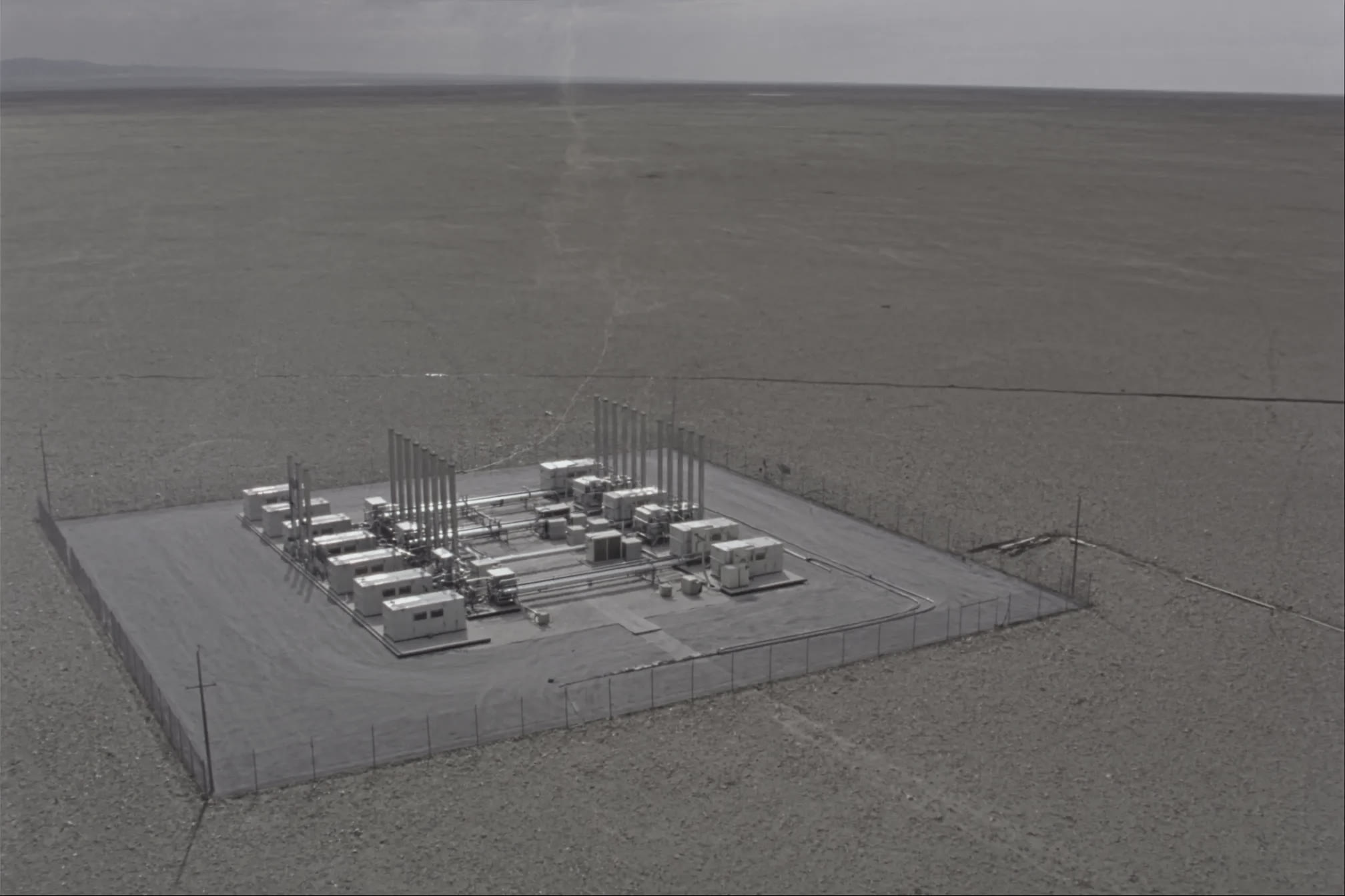High-oblique aerial of unbranded modular generation units on a fenced gravel pad.